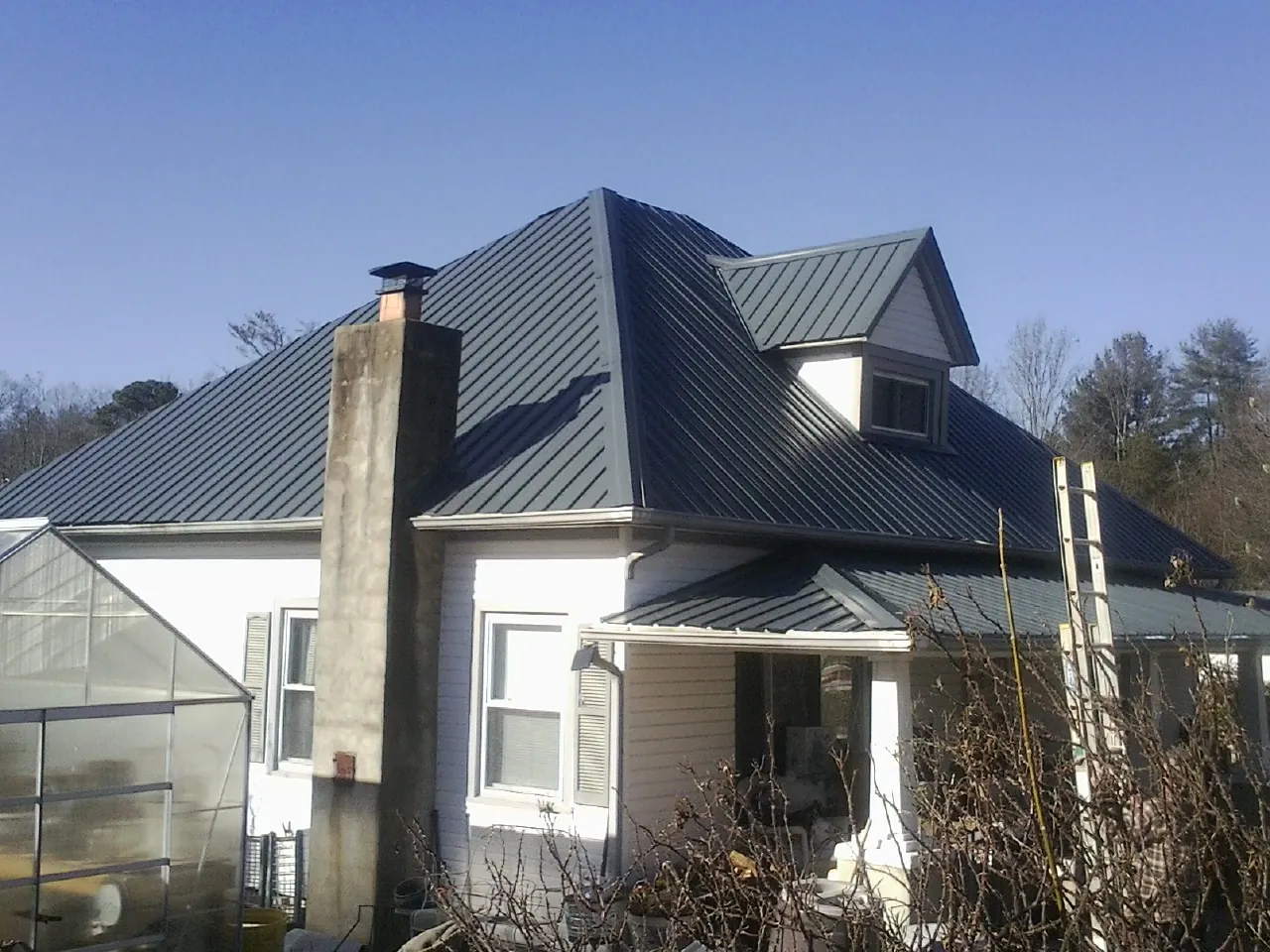 Dark blue standing seam metal roof on a white farmhouse with dormer — Slate & Tile Roof Repair by Roofing Brothers in Braman