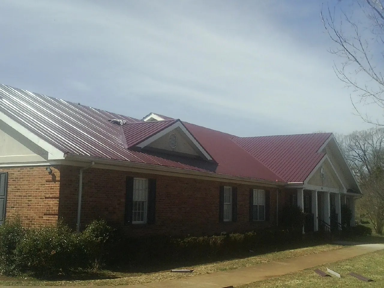 Red metal roof with gabled entries on a long brick building, from a Hail Damage Roof Repair job in Braman
