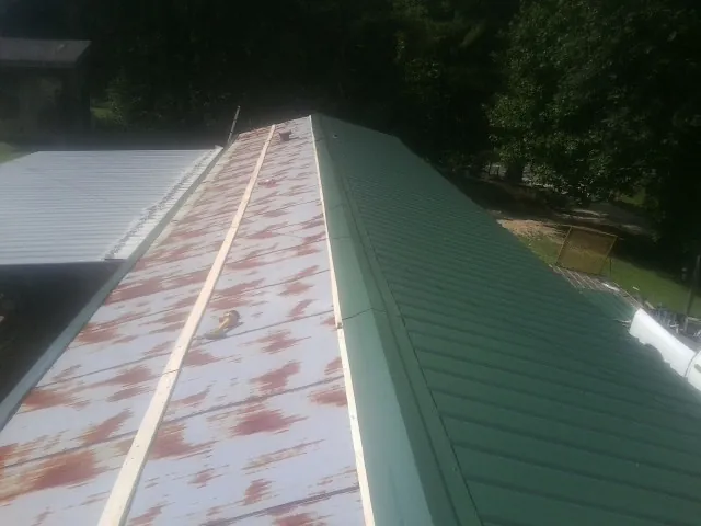 Old rusted panels beside newly installed green metal roofing — Wind Damage Roof Repair by Roofing Brothers in Braman
