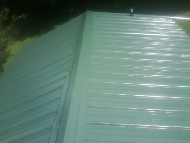 New green metal panels meeting at the ridge of a roof — Flat Roof Repair work by our crew in Braman