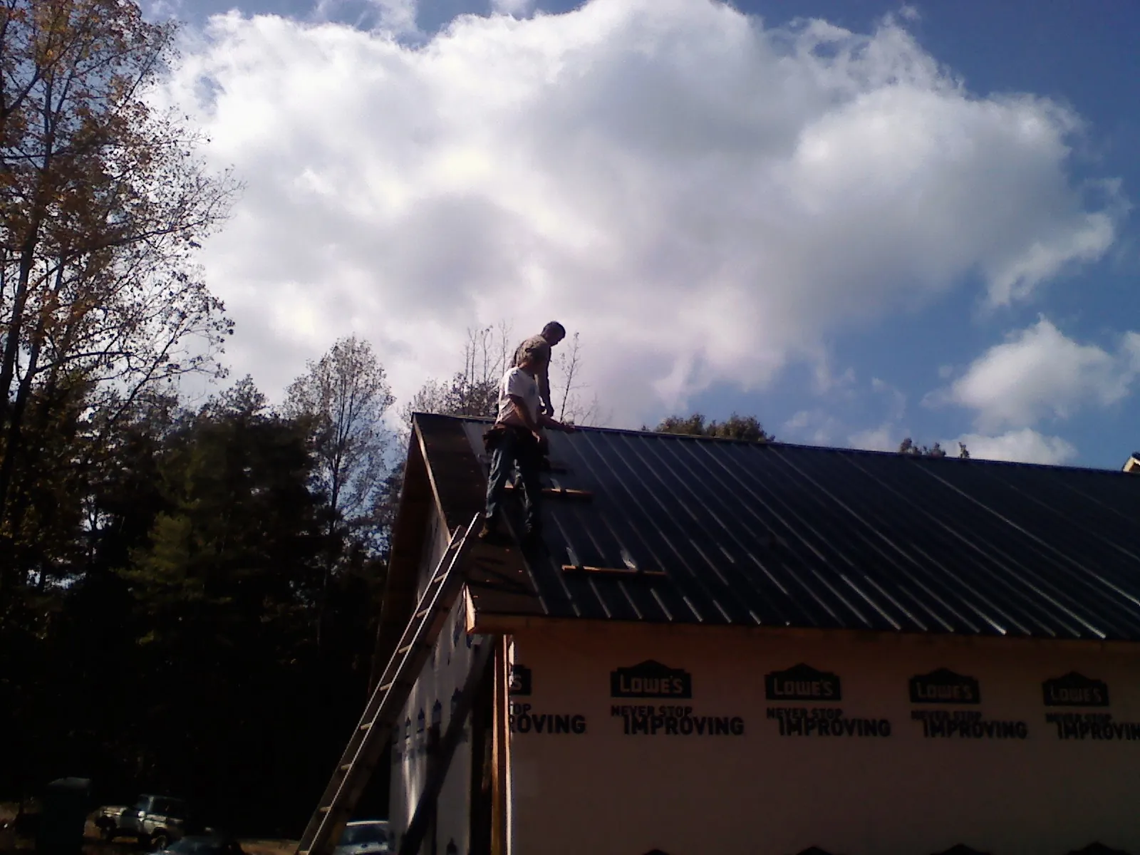 Roofer fastening dark metal panels high against a cloudy sky, from a Roof Inspection job in Braman