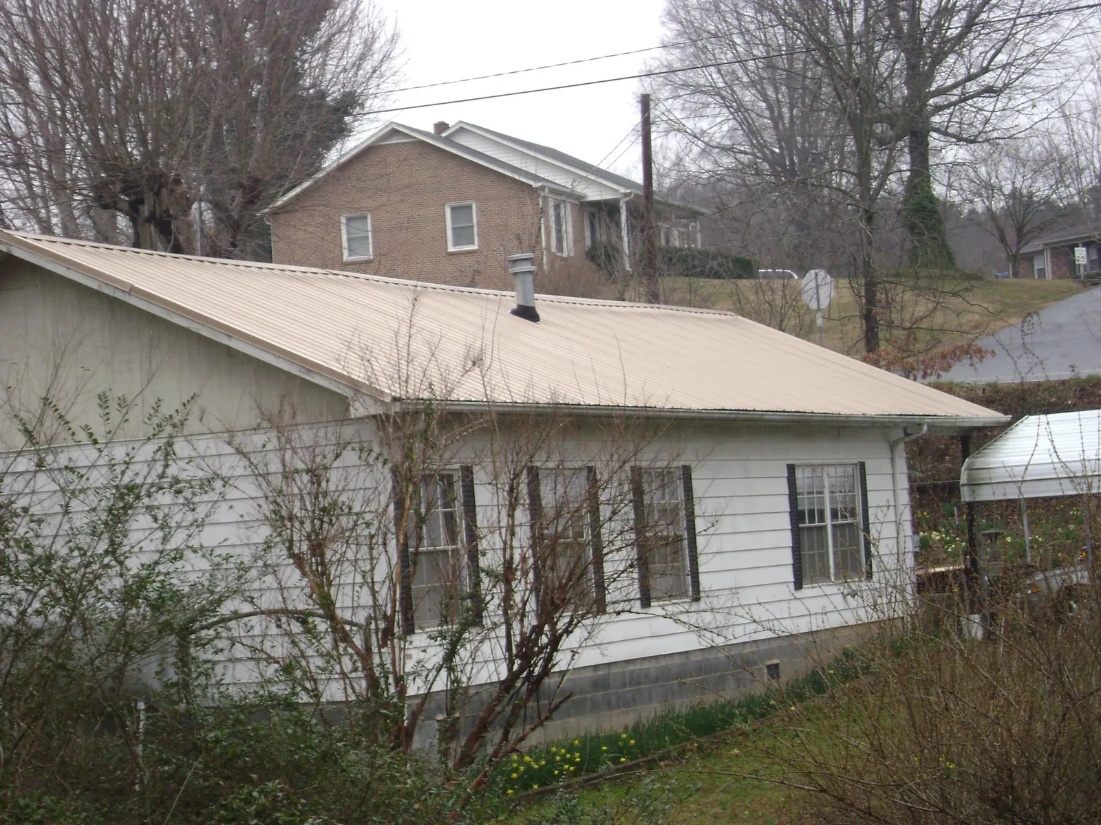 Tan metal roof on a white sided house set into a hillside — Commercial Roofing by Roofing Brothers in Braman