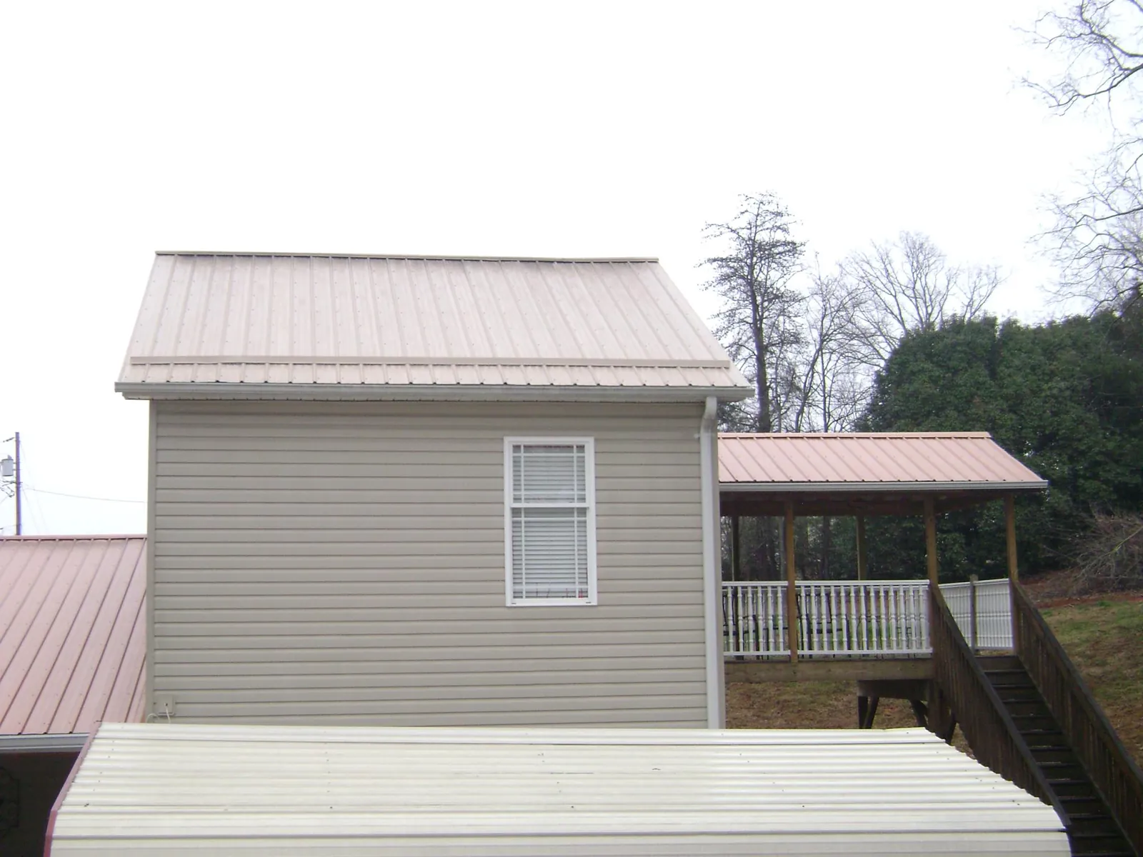 Tan metal roofs on a two story addition and attached porch, from a Roof Replacement job in Braman