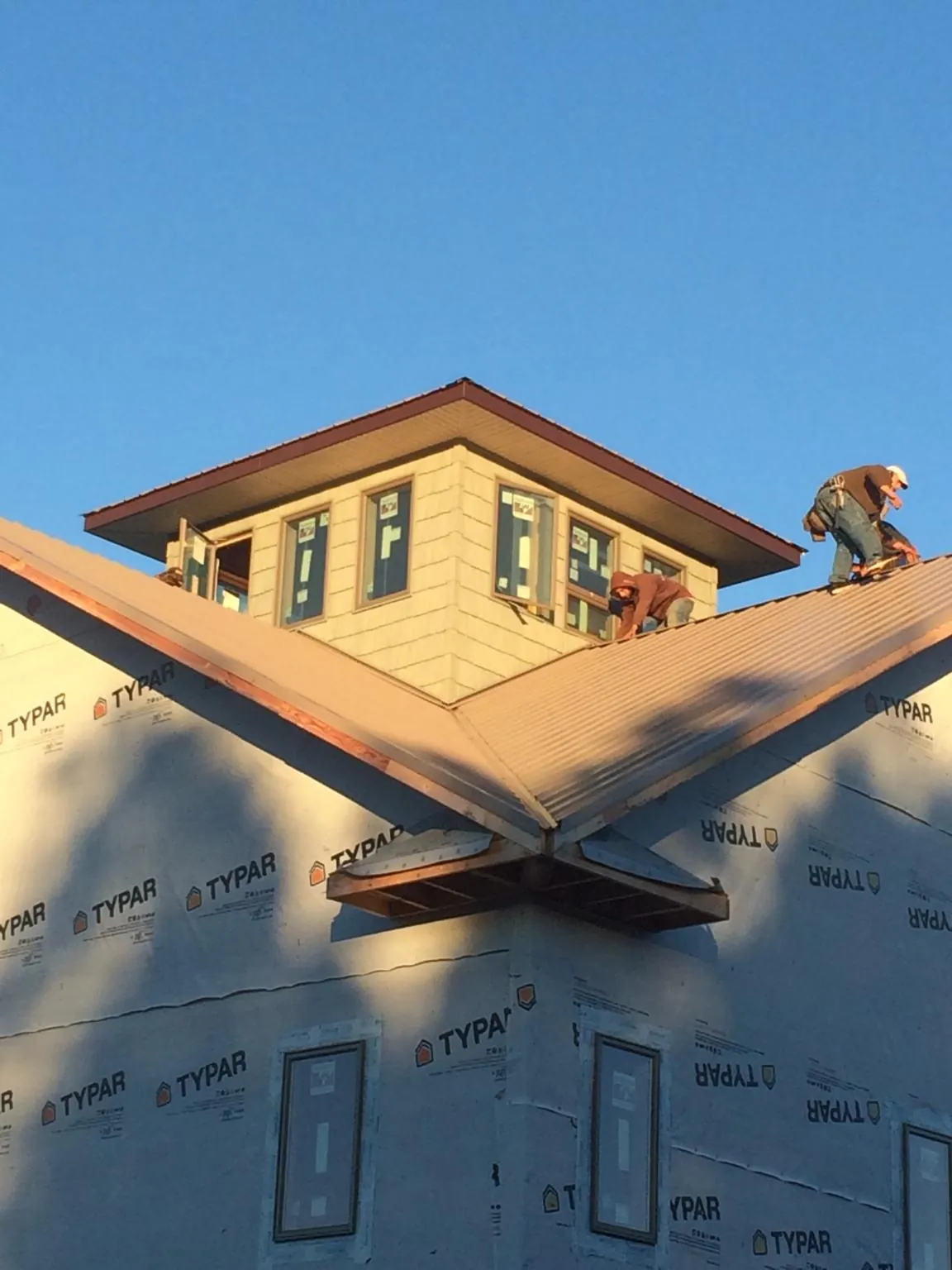 Roofers working around a rooftop cupola on a new metal roof at sunset — Roof Waterproofing in Braman by Roofing Brothers